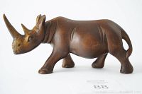 Side view of a dark brown hardwood rhino carving on a white background, showing detailed carving