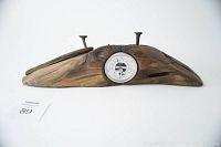 View from front showing the wood piece with barometer dial and three rusted nails protruding.