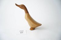 Side view of vintage wooden balsam duck figurine with darker head and lighter body, standing on two small feet.
