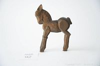 Side profile of small hand carved wooden donkey showing the angular faceted carving style and overall shape.