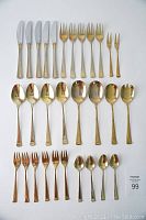 Top view of full gold plated cutlery set laid out on white surface showing all included pieces and their condition.