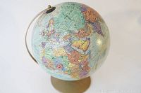 Full view of vintage earth globe showing Europe, Africa and Asia on a light blue ocean background with a gold-tone metal stand and meridian.