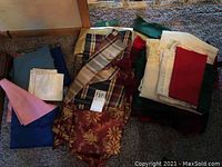Photo showing assorted folded tablecloths, runners, and napkins in various colors and patterns arranged on the floor.