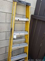 Full view of yellow fiberglass folding ladder leaning against wall, showing metal steps and overall structure.