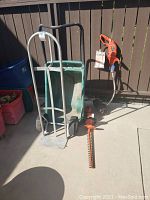Black & Decker corded hedge trimmer, weed wacker, garden cart, and hand dolly together outdoors in sunlight