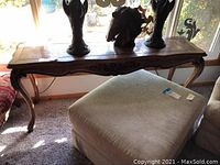 Long entry wooden table with carved legs seen next to window and upholstered furniture, showing scratches and general use