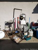 Wide view of lot showing step ladder, copper hanging pot on stand, propane tank, patio heater, metal baskets, Electrolux floor polisher, and assorted accessories.