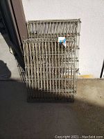 Stacked metal wire pet fencing panels leaning against a wall in outdoor space. Used for enclosure or pet containment.