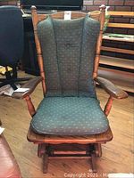 Full front view of the vintage wooden rocking chair with green cushioned upholstery showing the wood frame and tufted cushion.