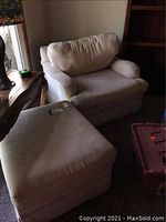 Photo of oversized upholstered chair and matching ottoman in a dimly lit room, showing overall condition and size relative to other furniture.