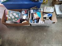 Wide shot showing two boxes filled with light bulbs and light fixtures on concrete floor.