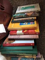 Stack of assorted books showing colorful and plain covers, including Mario Batali's The Babbo Cookbook and Cooks Illustrated editions