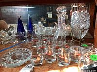Photo showing decanter, whisky glasses, ice bucket, and other glassware on a wooden surface in front of a mirror.
