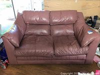 Front view of brown leather couch showing seat cushions and armrests with visible wear and tear