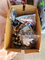 Cardboard box filled with toy figures and accessories in Ziploc bags.