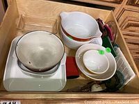 Drawer view showing mixed cookware assortment including ceramic and glass dishes plus metal bowl and kitchen linens.