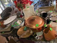 Overview of kitchen items including copper roaster, mixing bowls, mugs, and other items on table.