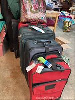 Photo showing the full lot of 5 suitcases and bags in stacked arrangement, includes plastic grocery bags on top and over the shoulder bag with floral pattern.