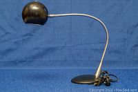 Front view of the mid century desk lamp showing the bent metal arm and spherical black shade with light scratches.