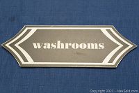 Front side of the vintage metal washroom sign showing gray paint background, white border and text 'washrooms'