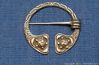 Close-up front view of the circular vintage silver brooch displaying Celtic knot and floral design detail on a blue fabric background.