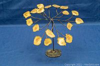 Front view of mid century metal tree sculpture on blue background showing yellow-painted metal leaves and metal base.