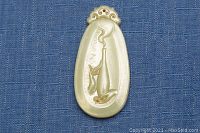 Top view of light-colored jade pendant with carved vessel and smoke motif on a blue fabric background
