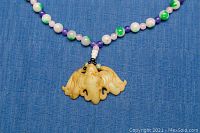 Close-up view of the carved bat pendant and multi-colored jade beads on the necklace.