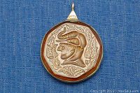 Front view of pendant showing carved amber with profile of man wearing horned hat and leaf motifs on blue fabric background.
