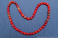 Full view of the old red Peking glass beaded necklace laid flat on a blue fabric background, showing the full length and bead arrangement.