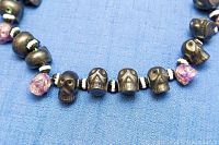 Close-up of multiple black skull-shaped beads and purple gemstone beads on the necklace