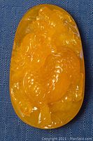 Front side of translucent yellow amber carved pendant with detailed dragon motif.