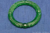 Front angled view of the carved jade bangle showing detailed dragon designs and the bead-like joint.