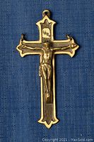 Old brass cross pendant with crucifix on blue textured background.