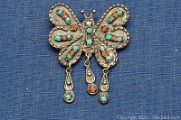 Front view of 925 sterling silver butterfly brooch with turquoise and coral inlaid stones and dangling silver elements.