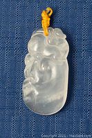 Front view of pendant showing carved mythical beast and swirl motifs on blue fabric.