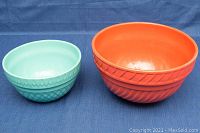 Two ceramic mixing bowls in light turquoise and orange with decorative exterior patterns on a blue background.