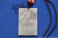 Close-up of front side showing the carved image of a man at a table with ornamental details on jade pendant