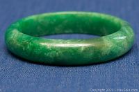 Side profile of the light green jade bangle showing polished surface and rounded shape on blue fabric