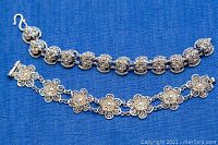 Two Mexican silver bracelets laid flat on blue cloth, showing front side with floral designs and clasp types.
