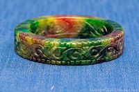 Close-up of carved side of multi-coloured jade bangle showing intricate swirl and geometric carving patterns in green, red, and yellow jade.