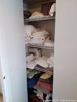 Closet shelves showing folded white sheets, pillow shams, towels, and multiple colorful crocheted afghans stacked on bottom shelf