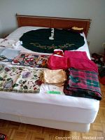 Photo showing Christmas linens spread on a bed including a green tree skirt, various cloth napkins, placemats, and towels.