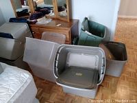 Photo showing most of the plastic bins arranged near furniture, some with lids open. Bins are gray and green plastic.