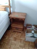 Night stand positioned next to bed showing wood finish, drawer handle, shelf and top surface.