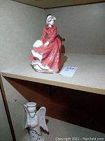 Porcelain figurine of a woman in a red dress seated on a shelf.