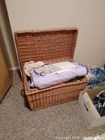 Photo showing open wicker trunk filled with folded quilts and linens placed inside.