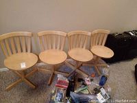 Four light wood swivel chairs with curved spindle backrests and cross-legged bases, lined up against a wall. Several miscellaneous items are placed in front of them, not included.
