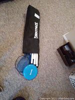 Black Spalding bag with badminton set including net and rackets, and blue Frisbee visible outside bag.