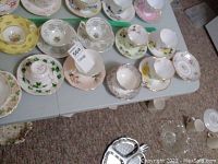 Photo showing full lot of teacups and saucers, various floral and patterned designs, including some yellow and pink tones.